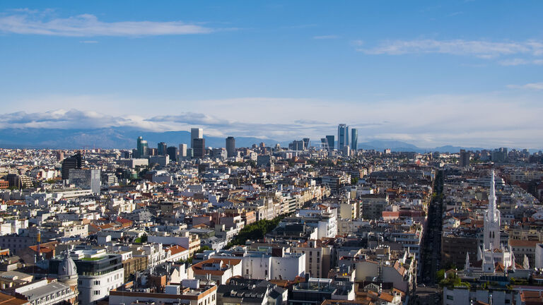 Es ist eine europäische Großstadt aus der Schrägluftperspektive zu sehen, der Himmel im Hintergrund ist blau mit kleineren Wolken
