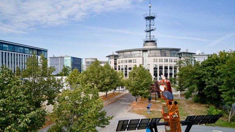 Es ist das Gebäude der EUMETSAT in Darmstadt zu sehen, vor dem Gebäude sind Modelle von Satelliten.