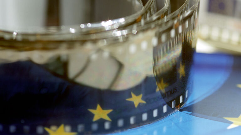 Es ist eine Filmrolle zu sehen, die auf einer EU-Flagge liegt.
