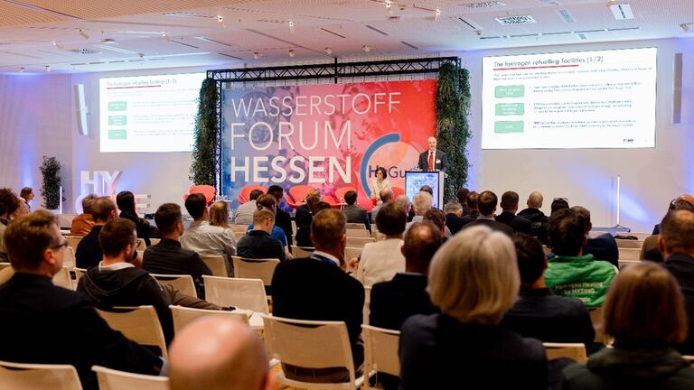 Vortrag der italienischen Delegation aus der Region Emilia-Romagna auf der Bühne, davor in Reihen sitzende Zuhörerinnen und Zuhörer