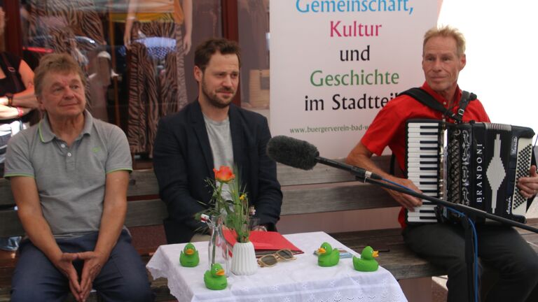 Das Foto zeigt Armin Ruda (Moderator), Jakob Benkhofer (TV-Schauspieler) und Welf Kerner (musikalischer Reisebegleiter) nebeneinander auf einer Bank sitzend