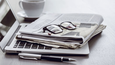 Zeitung und Brille liegen auf einem Laptop