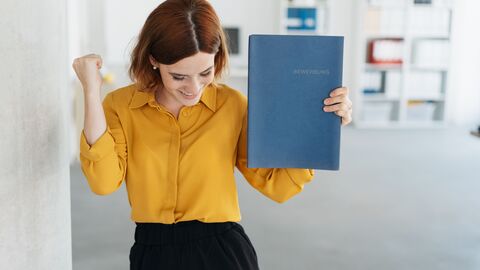 Eine junge Frau mit Mappe in der Hand freut sich Eine junge Frau mit Mappe in der Hand freut sich
