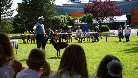 Vorführung mit einem Polizeihund und einem Polizisten in Uniform auf der Wiese beim Drillingstreffen 2021 - die Kinder sitzen im Kreis um die Wiese herum und schauen zu 