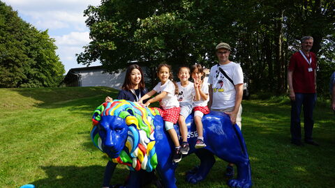 Kinder sitzen auf einer lebensgroßen blauen Hessenlöwen-Skulptur mit bunt bemalter Mähne