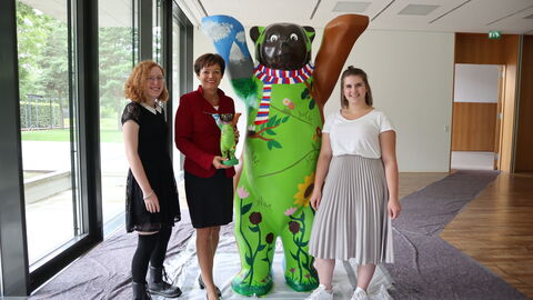 Gemeinsam mit der überlebensgroßen Bären-Skulptur schauen sie lächelnd in die Kamera: Staatsministerin Lucia Puttrich mit den Schülerinnen Mette Schombert (1.v.l.) und Amelie Ziersch (1.v.r.)