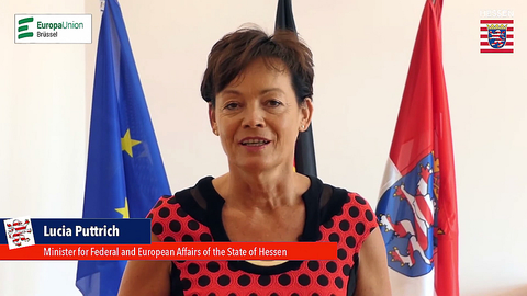 Lucia Puttrich spricht im Livestream vor dem Hintergrund mit Europafahne und Hessen-Fahne in die Kamera