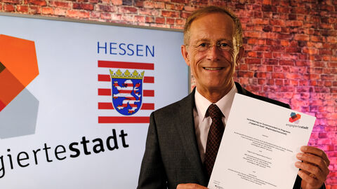 Staatsminister Axel Wintermeyer hält die Vereinbarung zur Zusammenarbeit im Programm "Engagierte Stadt" in die Kamera.