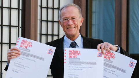 Staatsminister Axel Wintermeyer hält Förderbescheide in die Kamera