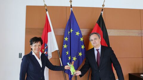 Staatsministerin Lucia Puttrich und Botschafter Francisco Ribeiro De Menezes halten einen kleinen bemalten Berlin-Bären in die Kamera