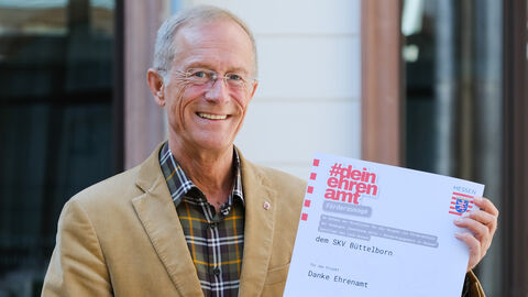 Staatsminister Wintermeyer hält den Förderbescheid für die SKV Büttelborn in den Händen und lächelt.