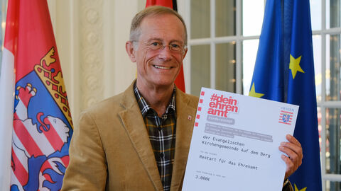 Staatsminister Axel Wintermeyer hält den Förderbescheid aus dem Programm "dein ehrenamt" in den Händen und lächelt.