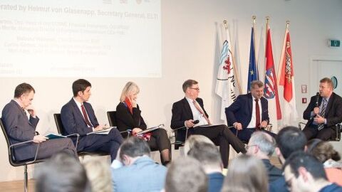 Teilnehmer der Podiumsdiskussion auf der Bühne sprechen miteinander