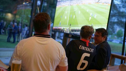 Das Foto zeigt Männer in Fußballtrikots vor einem großen Video-Bildschirm stehend, auf dem ein Fußballspiel übertragen wird: In der Hessenstube trafen sich Fußballfans, um das Europa-League-Finale live zu verfolgen