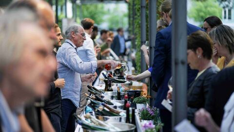 Gäste stehen in einer langen Warteschlange an einer Theke, an der Wein ausgeschenkt wird, im Garten der Hessischen Landesvertretung.. 