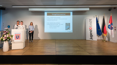 Drei Jugendliche stehen auf einer Bühne und halten eine Präsentation: Projekt "Mit Körpersprache zur 1+“: Lisa May (14), Emily Bauer (17) und Xenia Epp (17) aus Marburg gingen mit ihrem Projekt „Mit Körpersprache zur 1+“ das Problem des suboptimalen Vortragens von Präsentationen aufgrund einer ungeeigneten Körpersprache an.