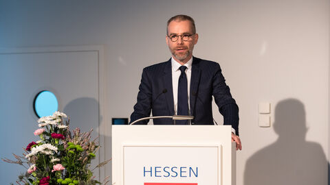 Ein Mann in einem Anzug steht vor einem Podium mit dem Hessenwappen darauf: Begrüßung Pascal Albrechtskirchinger, Leiter des ZDF-Europabüros Brüssel