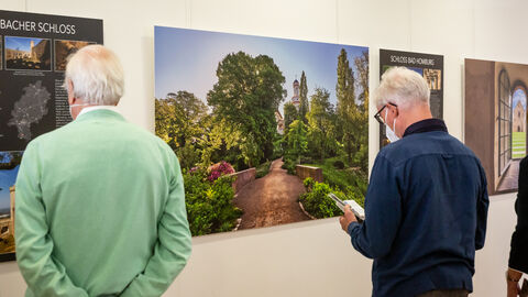 Gäste der Foto-Ausstellung stehen vor den an den Wänden aufgehängten großformatigen Farbfotos. Hier im Bild zu sehen ist das Schloss Bad Homburg