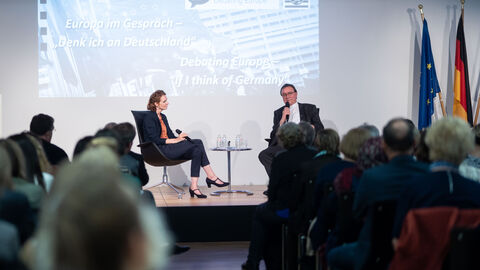 Eine Frau und ein Mann sitzen auf einer Bühne mit Mikrofonen in der Hand. Im Vordergrund sieht man Teile des Publikums von hinten: Franziska Broich, EU-Korrespondentin der Katholischen Nachrichten-Agentur im Gespräch mit Bischof Prof. Dr. Martin Hein