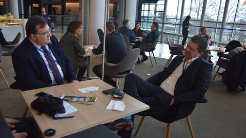 Mark Weinmeister und MdEP Sven Schulze Zwei Männer sitzen sich an einem Tisch gegenüber und unterhalten sich. Im Hintergrund sieht man weitere Menschen und Tische: Mark Weinmeister und MdEP Sven Schulze