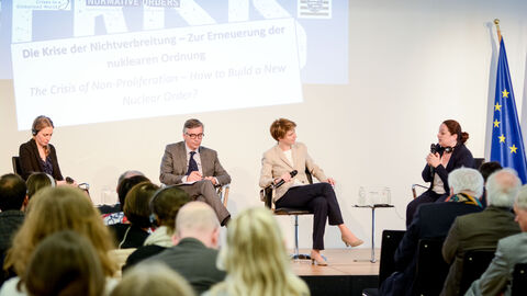 Mehrere Personen sitzen auf Stühlen auf einer Bühne und haben Mikrofone in der Hand: Podiumsdiskussion v.l.n.r.: Dr. Tytti Erästö, Prof. Dr. Christopher Daase, Moderatorin Astrid Corall und Elizabeth Konstantinova