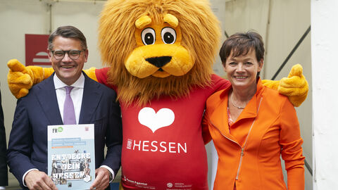 Ministerpräsident Boris Rhein und Staatsministerin Lucia Puttrich, in der Mitte ein überlebensgroßer Stoff-Löwe: Der Hessen-Löwe – das Landesmaskottchen der HA Hessen Agentur. 