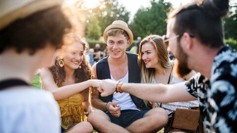 Eine Gruppe Jugendlicher sitzt zusammen auf dem Boden, alle strecken die Hände in die Mitte.