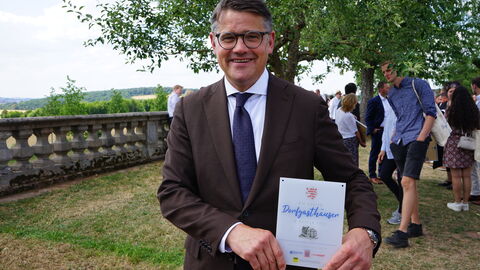 Fulda: Ministerpräsident Boris Rhein hat heute gemeinsam mit der DEHOGA Hessen die 50 Siegerinnen und Sieger des Wettbewerbs „Die besten Dorfgasthäuser in Hessen“ ausgezeichnet. Ministerpräsident Boris Rhein mit der Urkunde „Die besten Dorfgasthäuser in Hessen“ in den Händen lächelt in die Kamera.