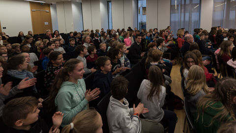 Vorlesewettbewerb 2019 Viele Kinder sitzen in Stuhlreihen und klatschen.