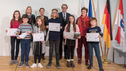 Vorlesewettbewerb 2019 Es sind sechs Kind zu sehen, die eine Urkunde in der Hand halten. Hinter ihnen stehen vier Erwachsene und die Flaggen von Europa, Deutschland und Hessen. Alle lächeln in die Kamera.