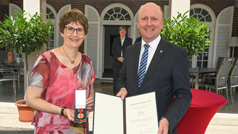 Marion Beier und Europastaatssekretär Uwe Becker halten Verdienstmedaille und Urkunde in die Kamera