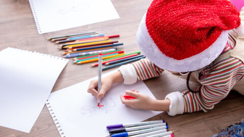 Malendes Kind Ein Mädchen mit Weihnachtsmann-Mütze malt mit Buntstiften auf weißem Papier.