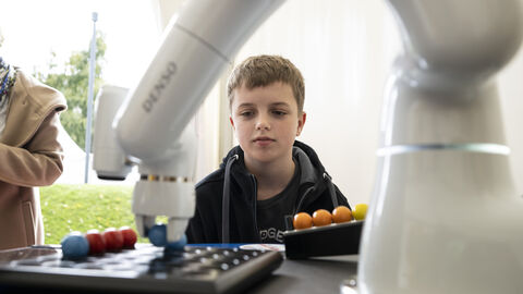 Ein kleiner Junge betrachtet einen Roboterarm bei der Arbeit: Was passiert denn hier?...