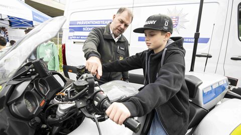Ein Junge sitzt auf einem Polizeimotorrad und ein Polizist gibt ihm Informationen