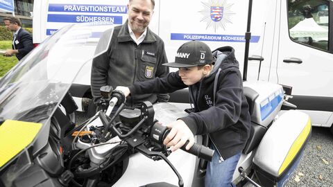 Ein Junge sitzt auf einem Polizeimotorrad, ein Polizist steht lächelnd neben ihm