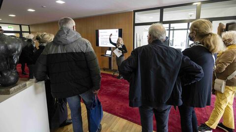 Was genau sind denn die Aufgaben einer Landesvertretung? Bei Rundgängen durch die Landesvertretung durften Gäste einen Blick hinter die Kulissen werfen: Menschen stehen vor einem Bildschirm in der Landesvertretung und erhalten eine Erläuterung zu einer Präsentation von einer Mitarbeiterin