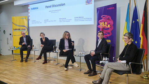 Podiumsdiskussion zum EU Chips Act Podiumsdiskussion mit fünf Teilnehmern, die einander zugewandt auf Stühlen auf der Bühne vor einer großen Leindwand sitzen.