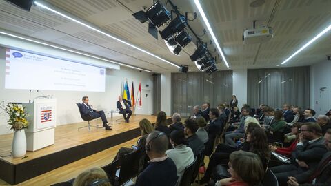 Ein Blick ins Publikum - zu sehen ist eine große Halle in der viele Zuschauer auf Stühlen sitzen und zur Bühne schauen, auf der die Diskussion stattfindet