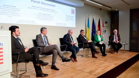 Podiumsdiskussion Die Teilnehmer der Podiumsdiskussion sitzen auf Stühlen nebeneinander auf der Bühne und schauen lächelnd ins Publikum