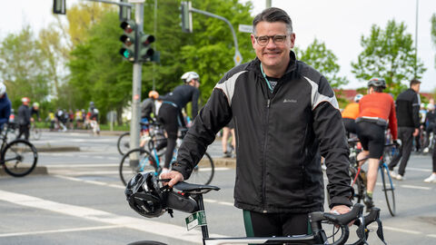 Ministerpräsident Rhein steht neben seinem Rennrad und lächelt in die Kamera