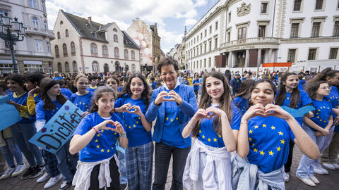Lucia Puttrich mit Teilnehmerinnen und Teilnehmern des Flashmobs auf einem Platz in Wiesbaden, alle machen mit den Händen ein Herz-Zeichen.