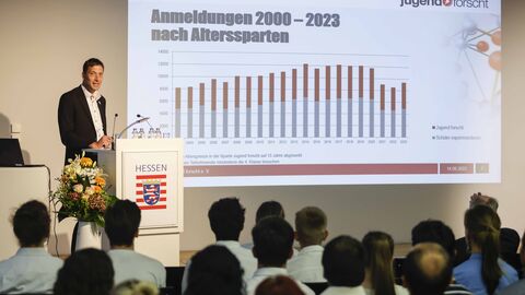 Person spricht auf der Bühne, erläutert eine an die Wand projizierte Statistik von Jugend forscht