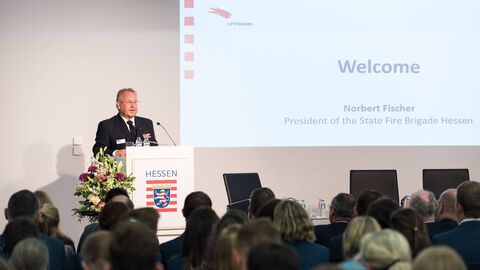 Norbert Fischer, Präsident des Hessischen Landesfeuerwehrverbandes Am Rednerpult vor einer Leinwand mit PowerPoint-Präsentation spricht Norbert Fischer, Präsident des Hessischen Landesfeuerwehrverbandes, zu den Gästen