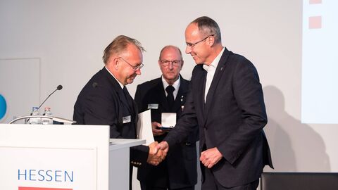 Minister Peter Beuth und Norbert Fischer Schütteln Hände und lächeln am Rednerpult: Minister Peter Beuth und der Präsident des Hessischen Landesfeuerwehrverbandes