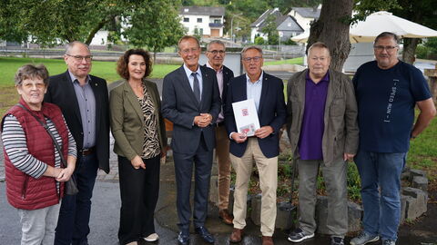 Staatsminister Wintermeyer mit mehreren Personen unter Bäumen, er übergibt einen Förderbescheid.