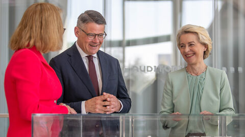 Ministerpräsident Rhein und Ursula von der Leyen stehen gemeinsam vor einem Kasten mit einem Modell. Sie unterhalten sich mit einer dritten Person.