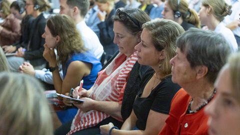 Zahlreiche Besucher sind zu sehen, die gespannt und aufmerksam nach vorne schauen