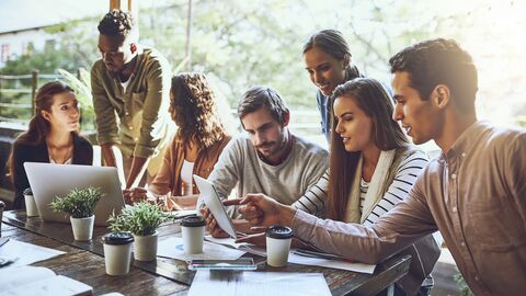 Sieben Jugendliche sitzen unterhaltend am Tisch, vor ihnen stehen zwei Laptops