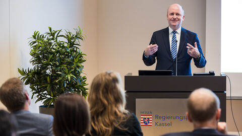 Europastaatssekretär Uwe Becker erläutert die Aktivitäten der Hessischen Landesregierung anlässlich der Europawahl Europastaatssekretär Uwe Becker steht am Rednerpult und gestikuliert, Teile des Publikums sind im unteren Bildausschnitt von hinten zu sehen.