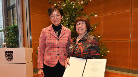 Staatsministerin Lucia Puttrich und Annemarie Jonas lächeln in die Kamera. Frau Jonas hält ihre Auszeichnung vor ihrem Oberkörper.